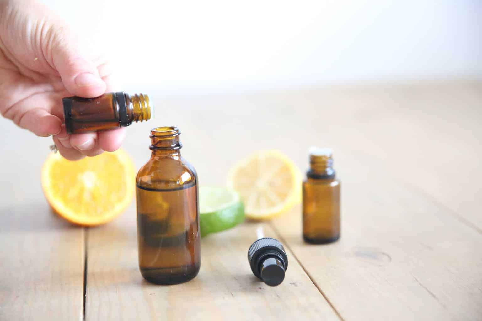 adding essential oils to a perfume bottle. with lime and lemon slices on wooden table