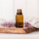 Amber colored essential oil bottle on wooden cutting board with lavender sprigs behind it.