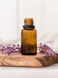 Amber colored essential oil bottle on wooden cutting board with lavender sprigs behind it.