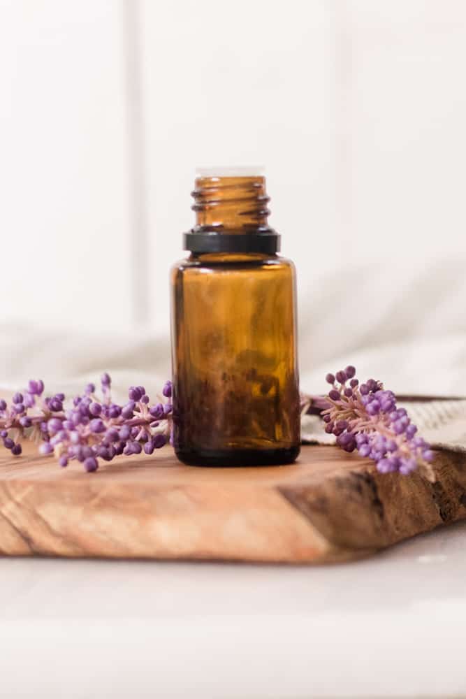 lavender essential oil bottle on wooden cutting board with lavender sprigs behind it.