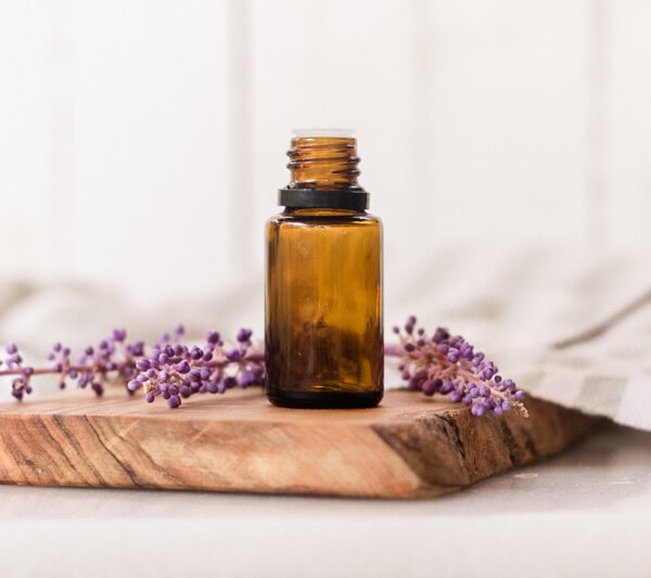 Amber colored essential oil bottle on wooden cutting board with lavender sprigs behind it.