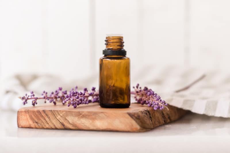 Amber colored essential oil bottle on wooden cutting board with lavender sprigs behind it.