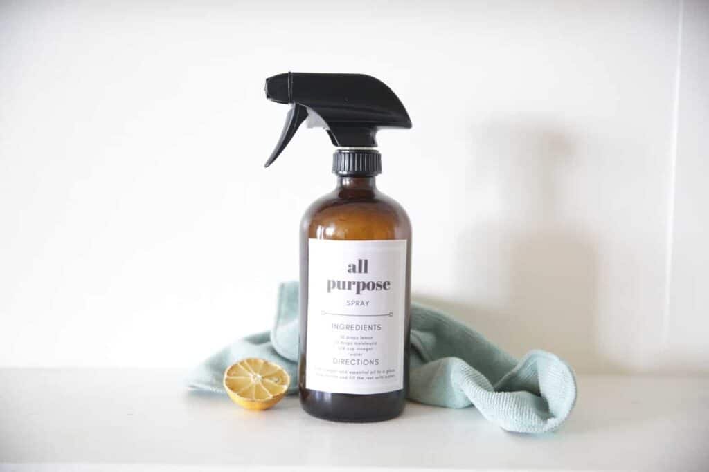 DIY all-purpose spray in reusable glass spray bottle. Surrounded by dried lemons and a microfiber towel on white marble vanity.