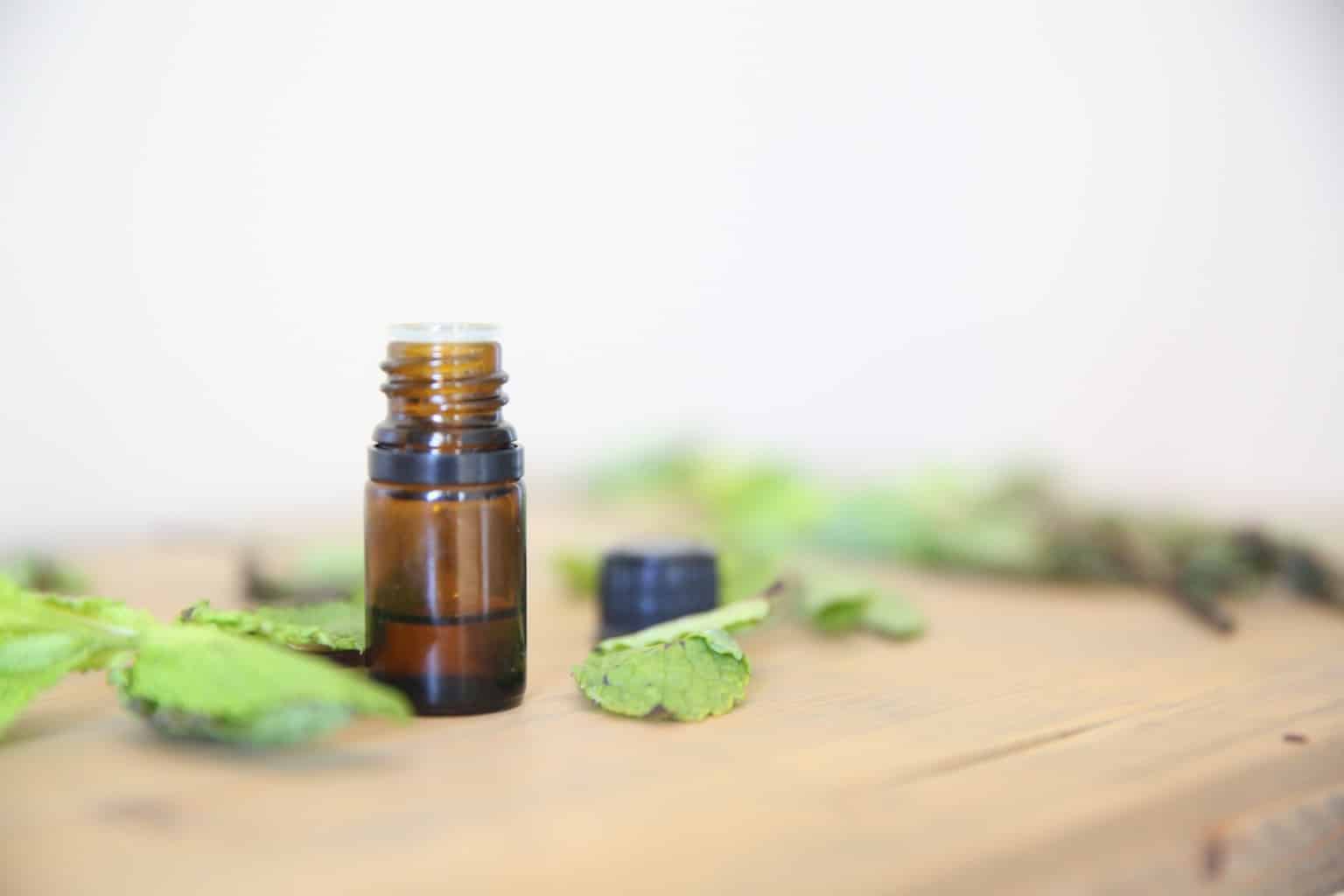 Amber essential oil bottle on wooden table with peppermint leaves.