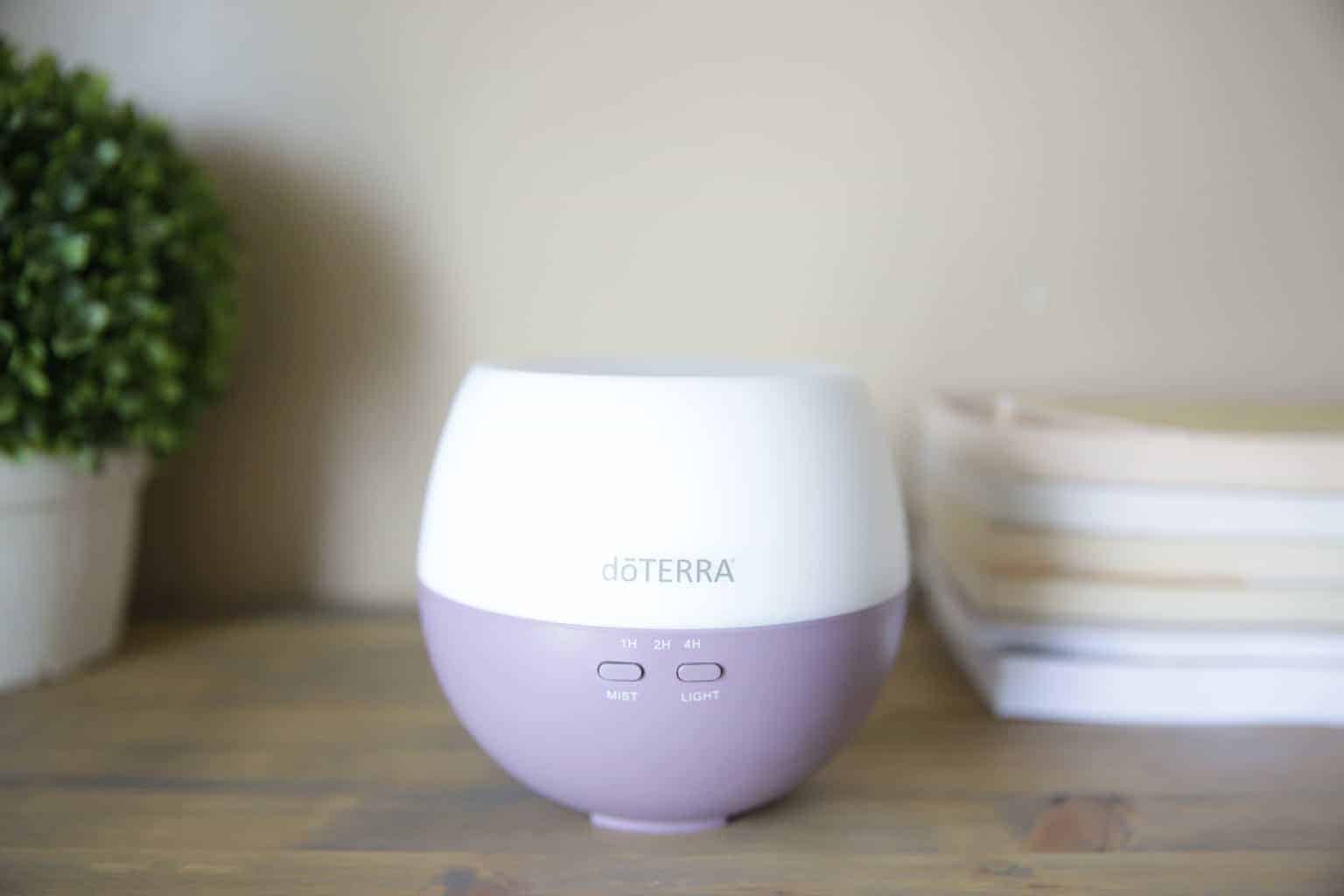 doTERRA essential oil diffuser on wooden end table next to decorative green bush