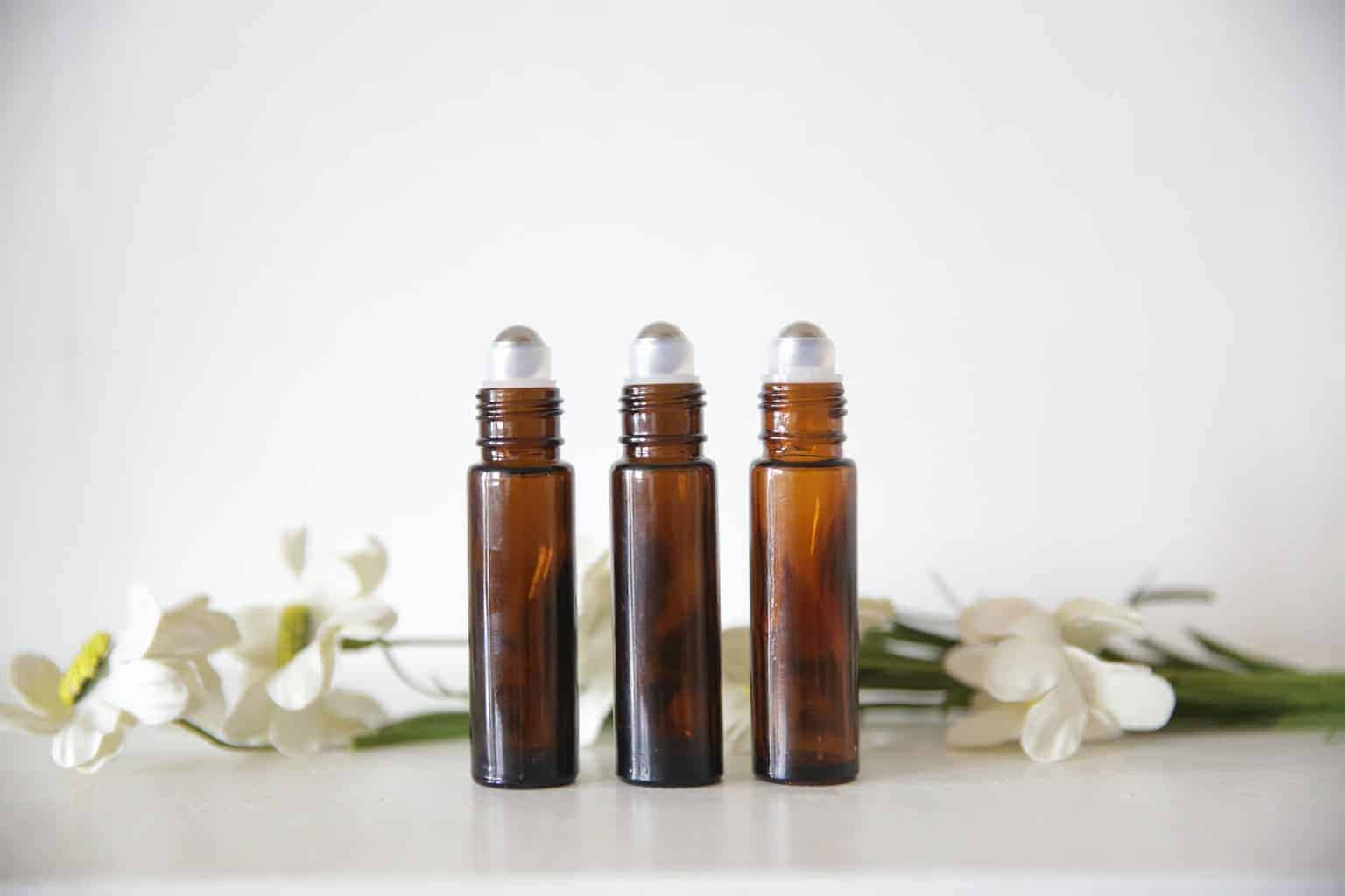 Roller bottles surround by fresh flowers on white table.