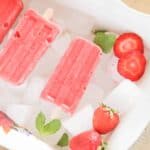 red popsicles strawberry slices and peppermint leaves on ice.