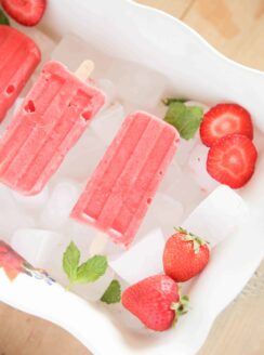 red popsicles strawberry slices and peppermint leaves on ice.