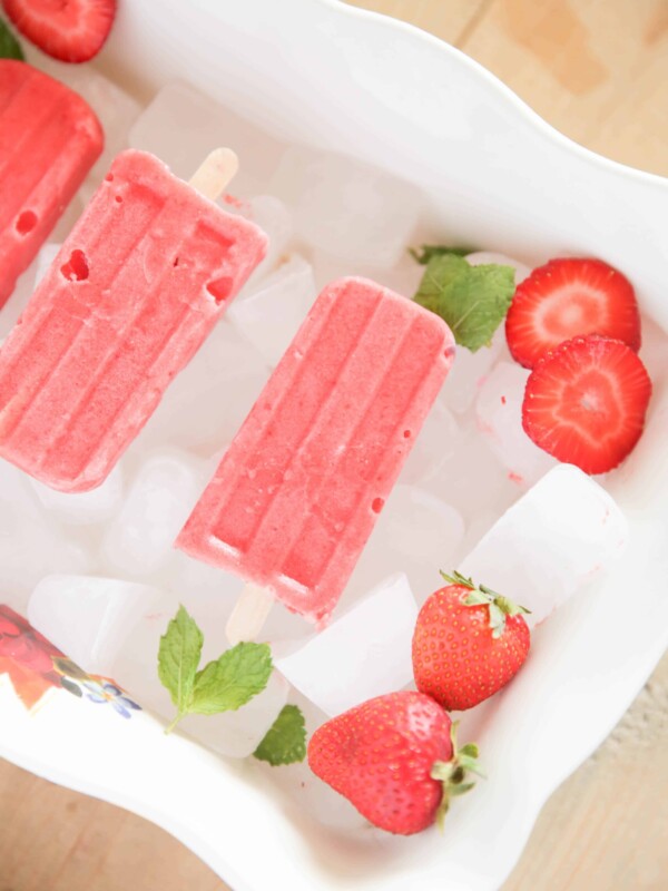 red popsicles strawberry slices and peppermint leaves on ice.