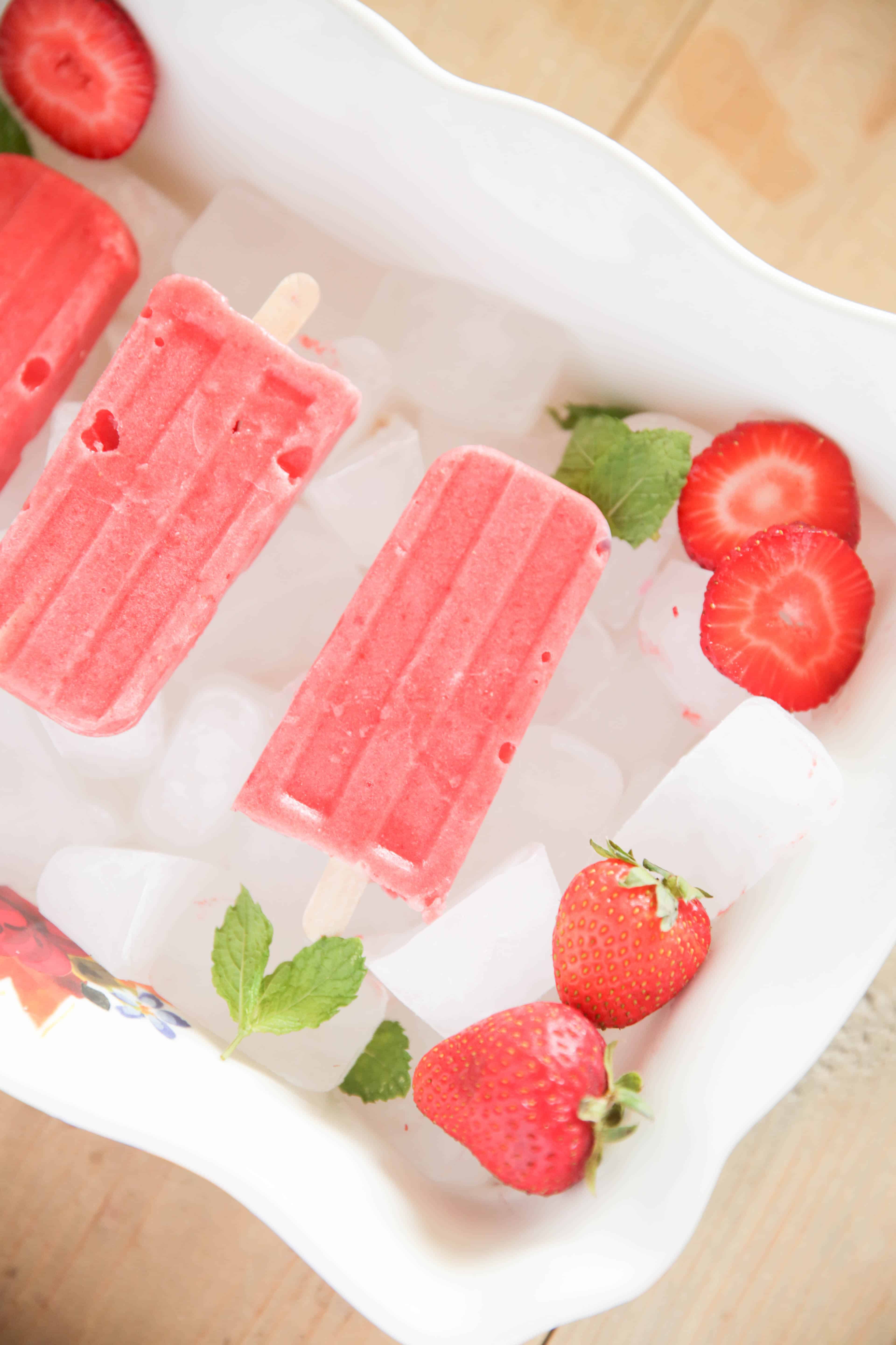 red popsicles strawberry slices and peppermint leaves on ice