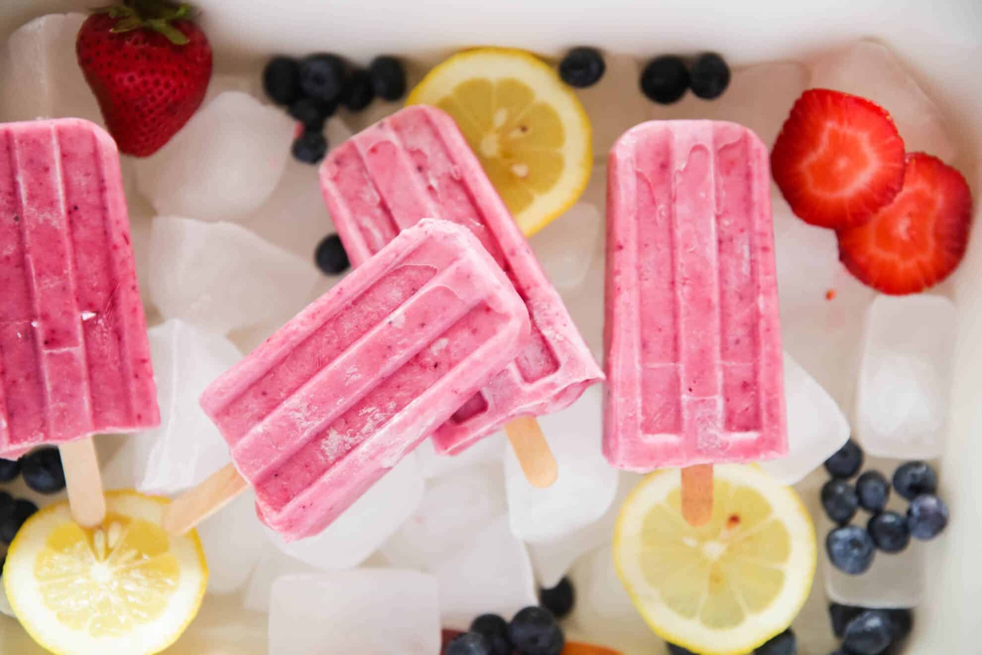 Berries lemon slices and pink popsicles on ice.