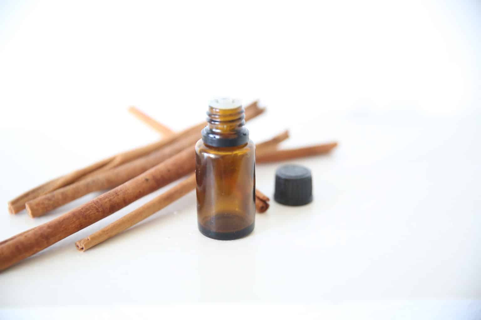 cinnamon essential oil bottle with cinnamon sticks on white marble