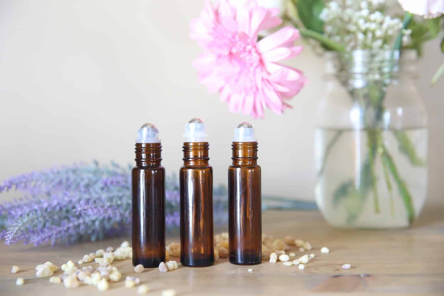 Essential oil roller bottles on wooden table with fresh flowers.