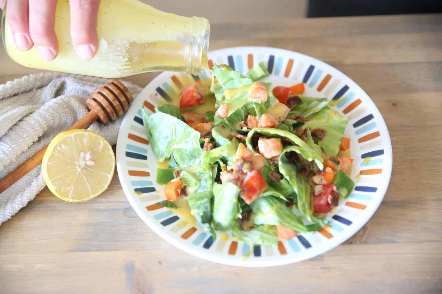 pouring homemade lemon honey mustard on salad from a glass jar