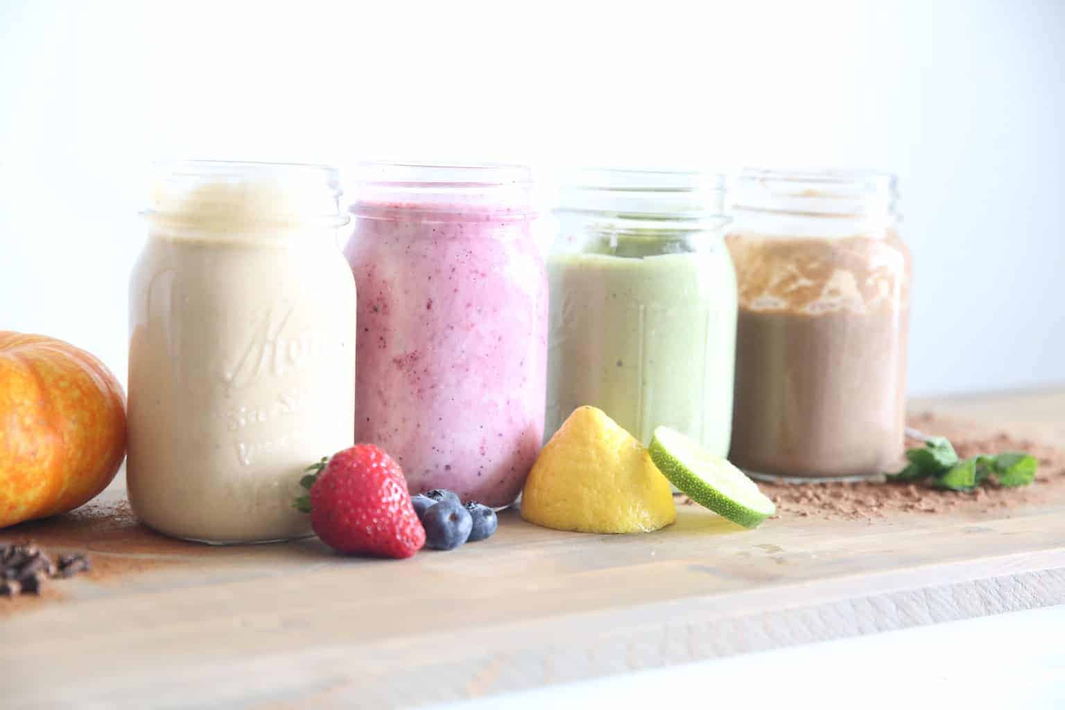 5 Healthy Smoothies with Essential Oils in 1 qt glass mason jars. fresh fruit laid around the base