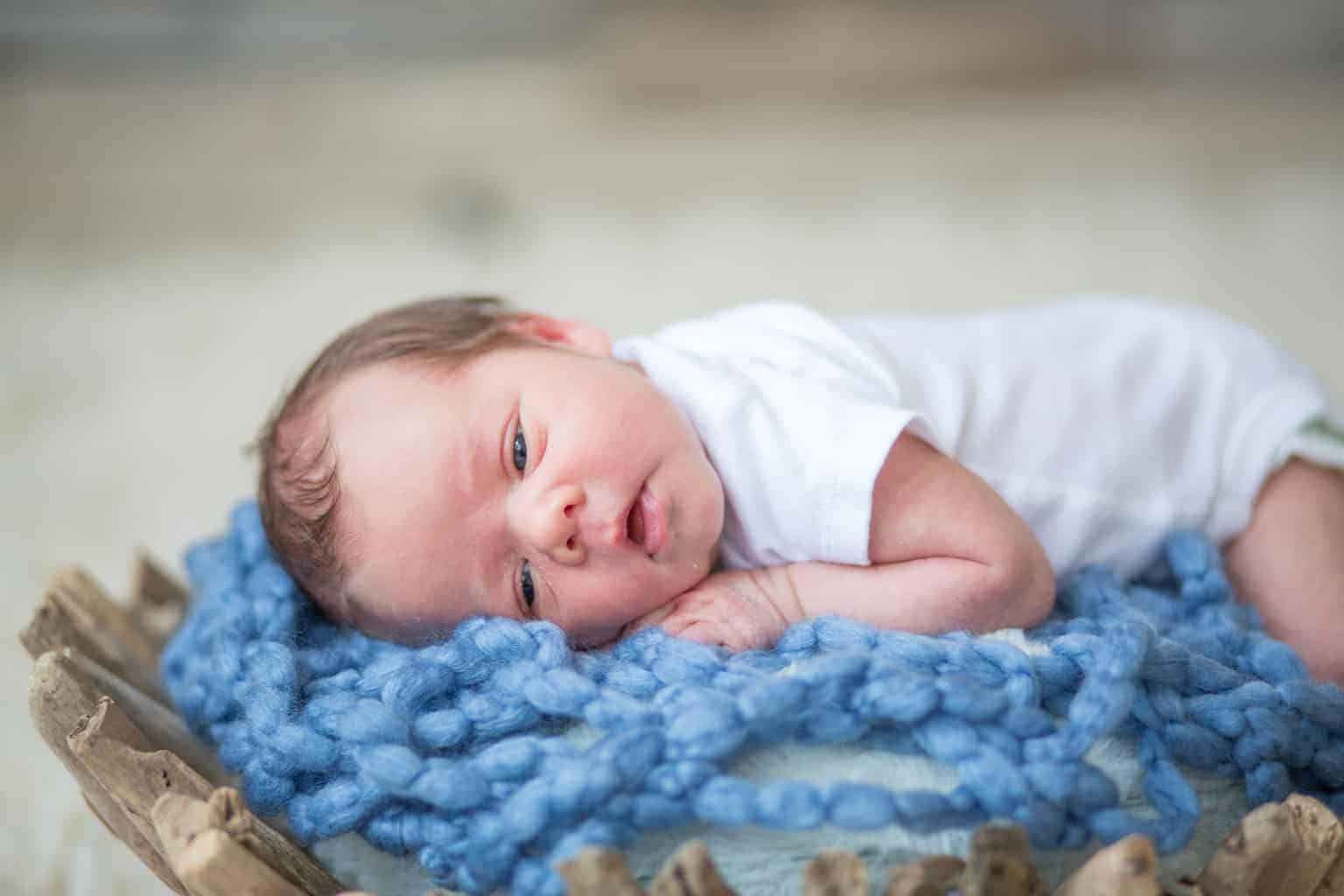 Baby boy in basket with blue knit blanket.