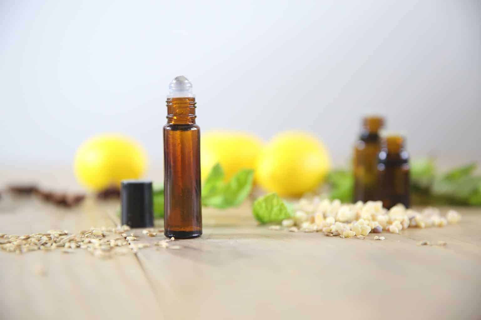 Essential oil roller bottle on wooden table with lemons in background.