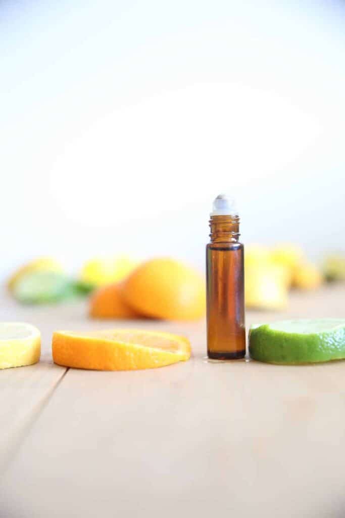 Essential oil roller bottle with sliced citrus fruits in background.
