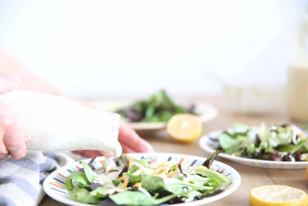 Pouring homemade healthy ranch dressing on a fresh salad.