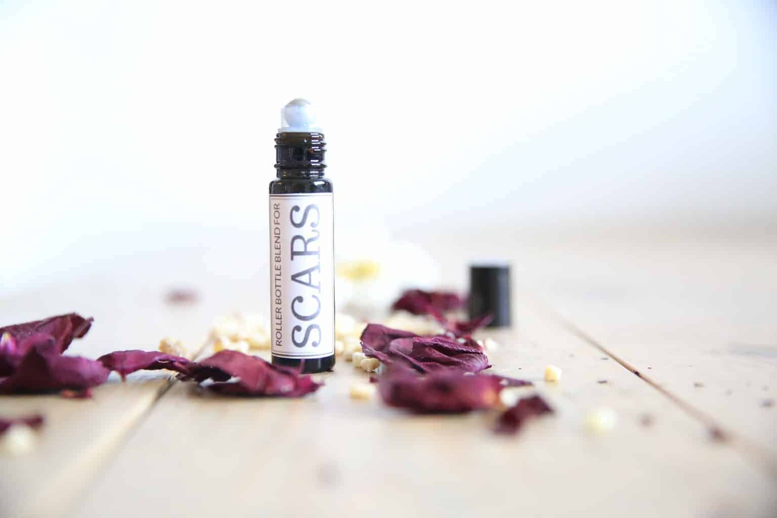 Scar essential oil roller bottle with rose petals around it.