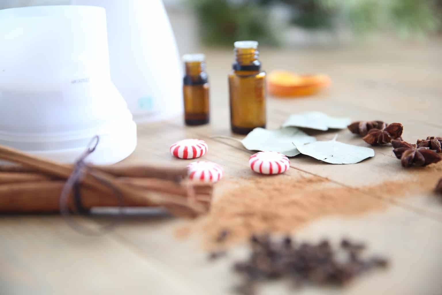 Oil diffuser, cinnamon sticks, oil bottles and peppermint candy on wooden table.