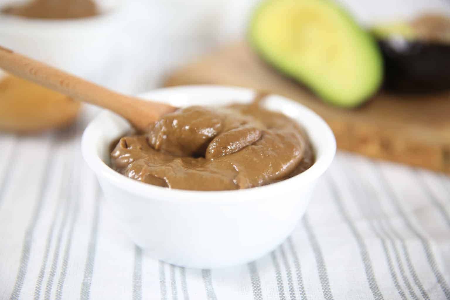 Chocolate avocado pudding in white bool on table cloth.