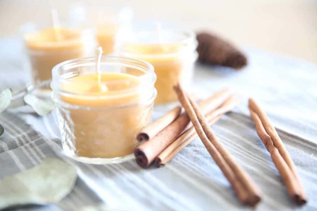 Homemade beeswax candles with cinnamon sticks in glass jars.