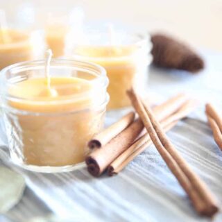 Homemade beeswax candles with cinnamon sticks in glass jars.