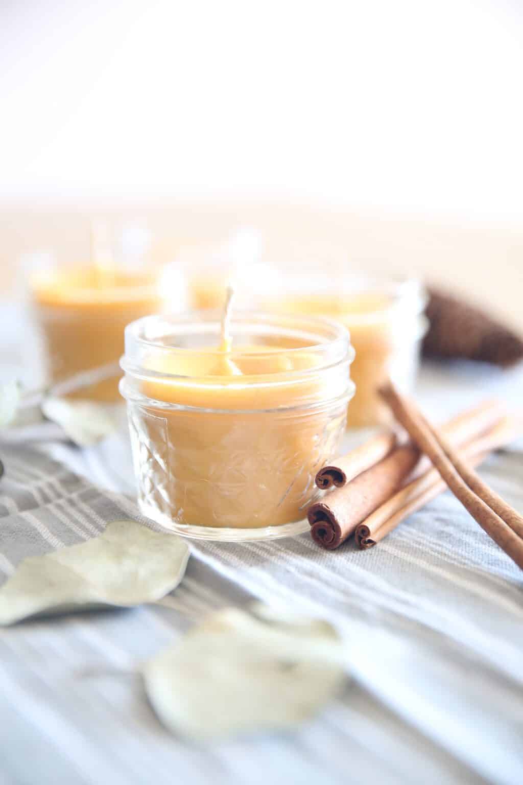 Beeswax candles in little mason jars on grey table cloth.