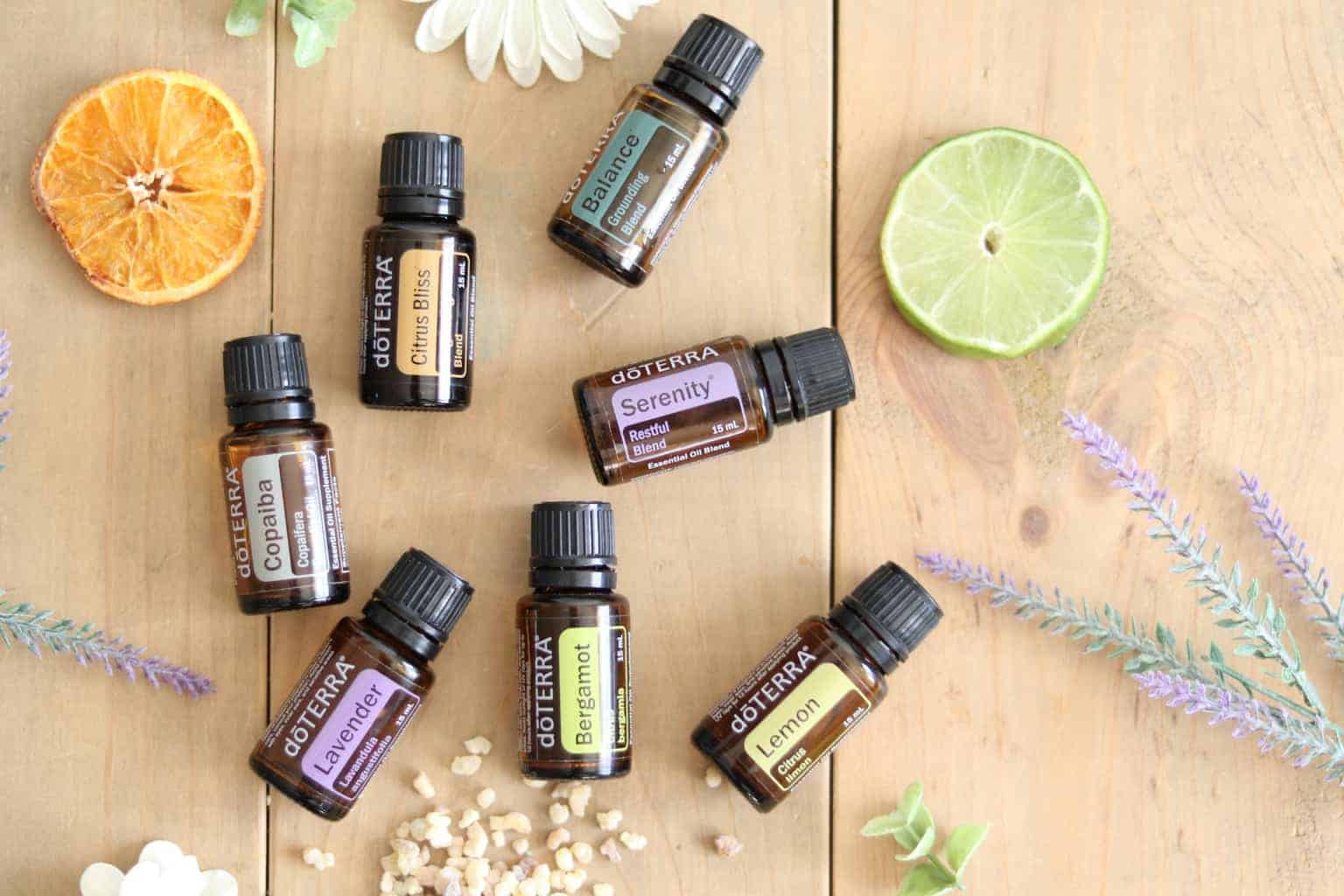 Essential oil roller bottles with dried flowers and fruits on wooden table.