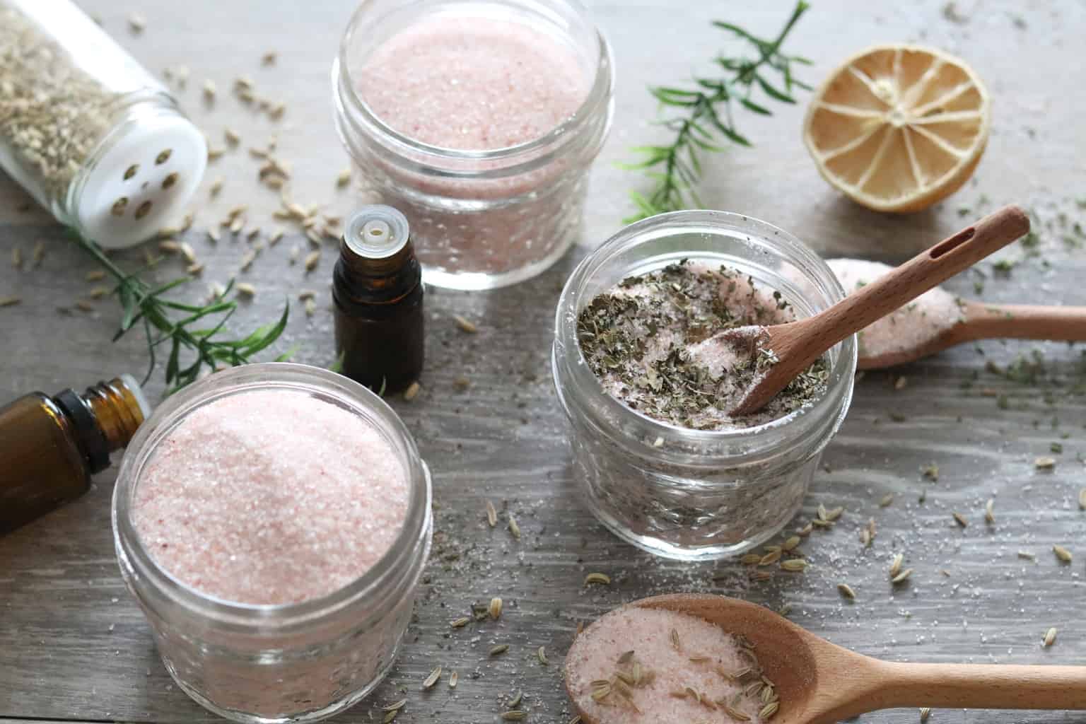 Oil infused seasoning salts in small mason jars on table with oil bottles, and wooden spoons.