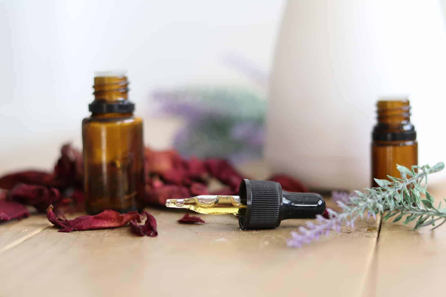 Roller bottles, dried flowers and oil diffuser on wooden table.