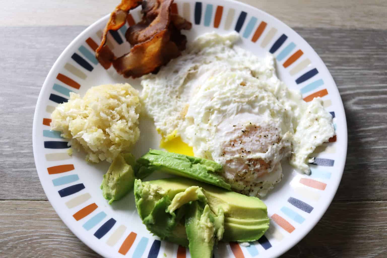 Fried egg, avocado and bacon on plate.