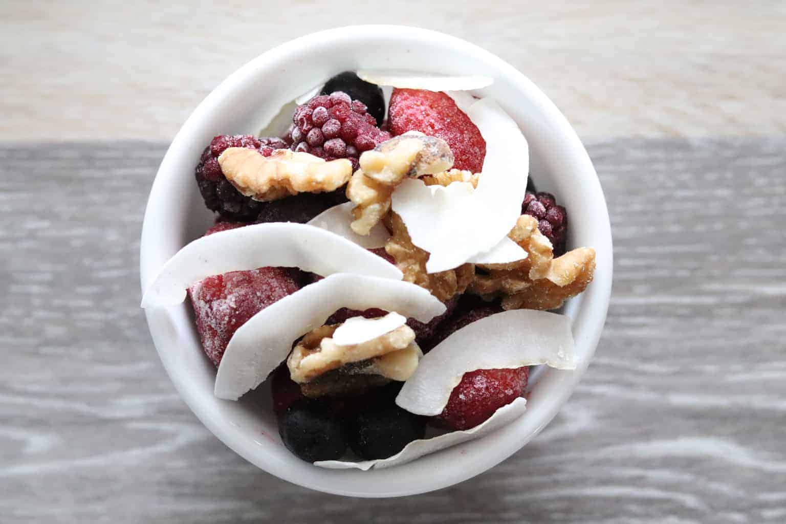 Frozen fruit, mixed nuts, and shredded coconut in bowl.