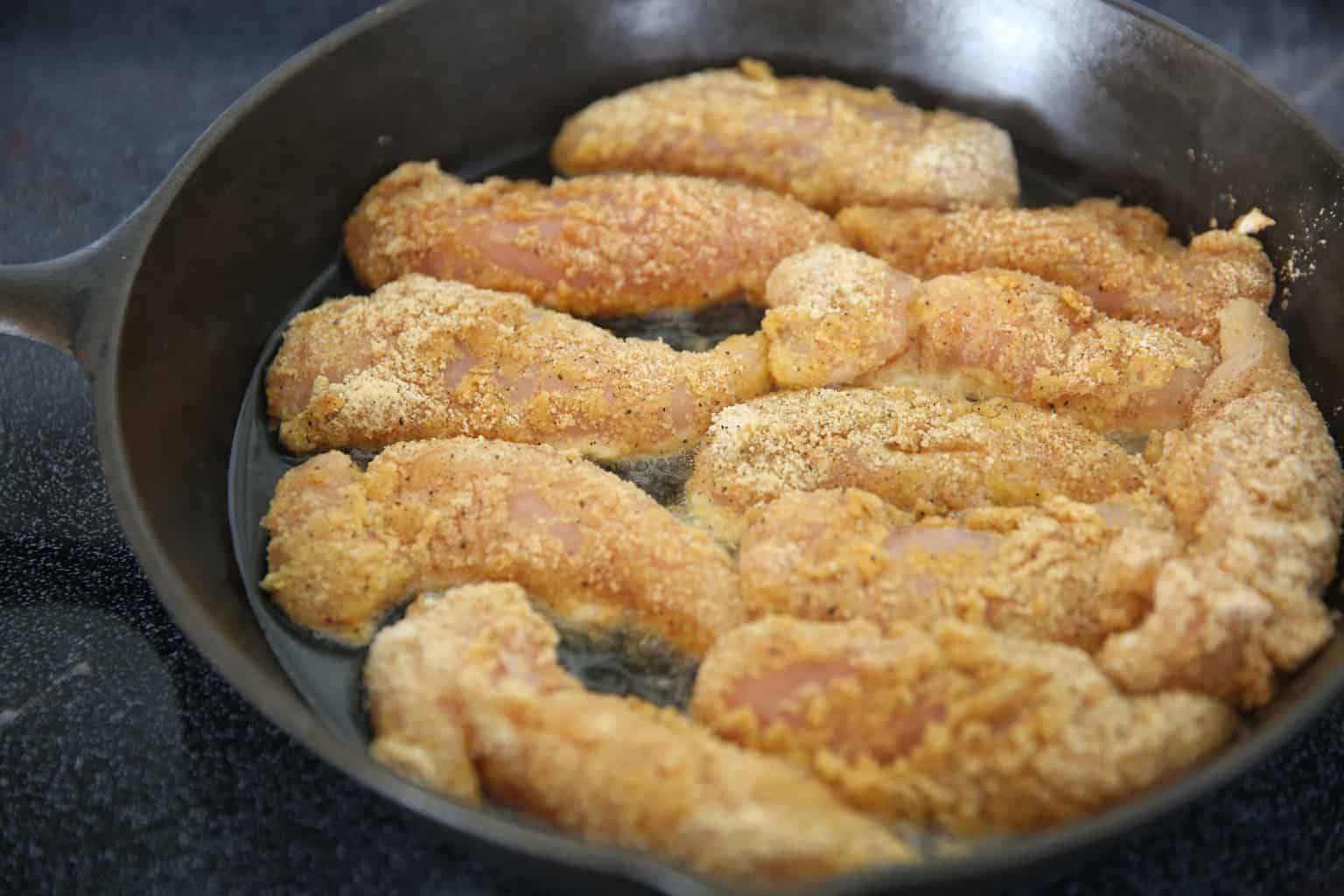 Frying chicken strips in cast iron skillet.