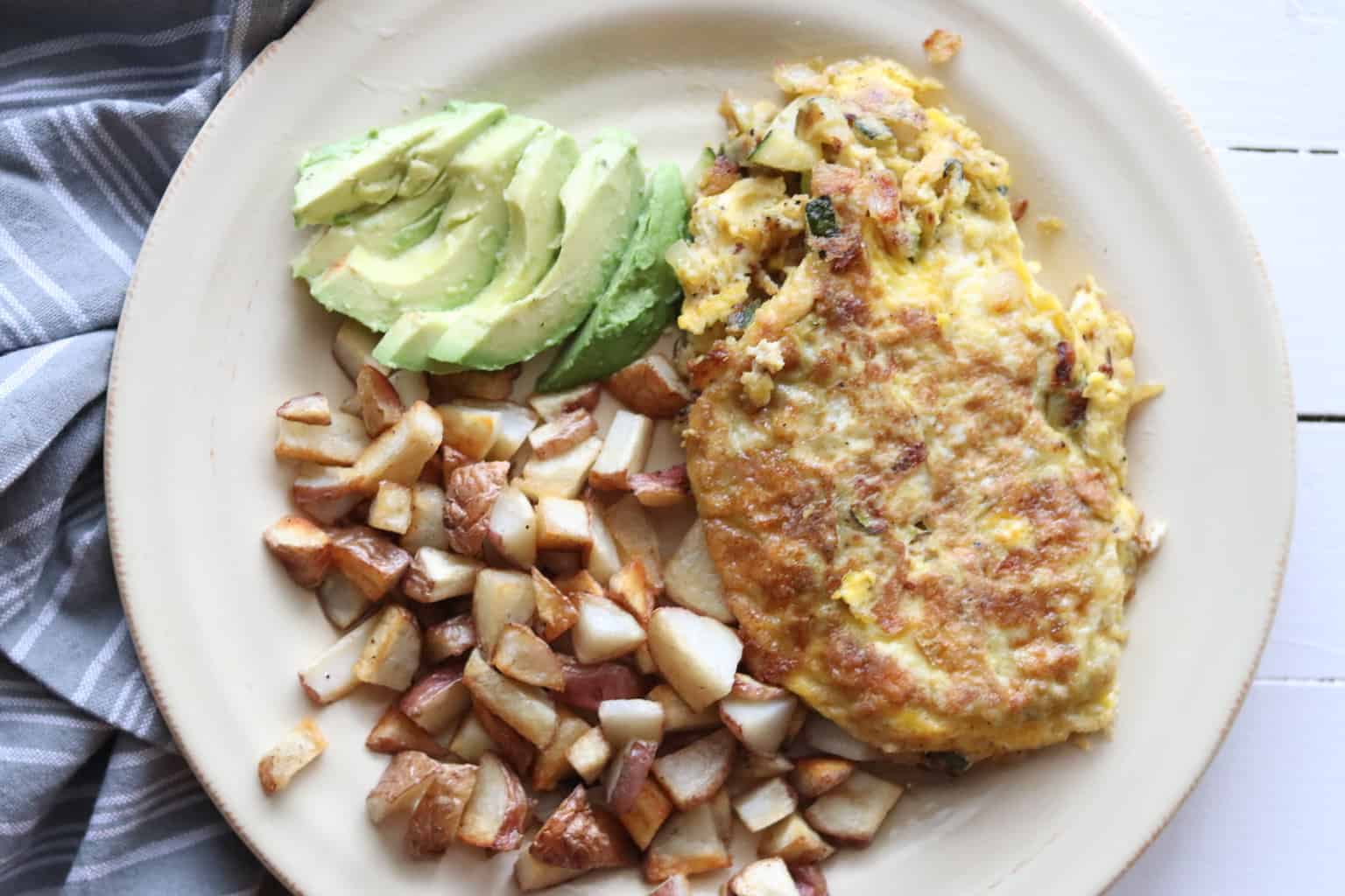 Vegetable omelet served with hash browns, avocados, and sauerkraut.