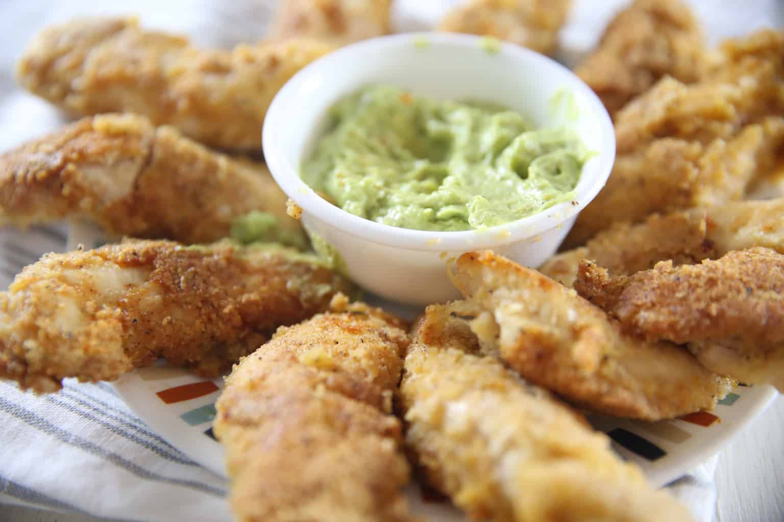 Chicken strips with avocado dipping sauce on white plate.