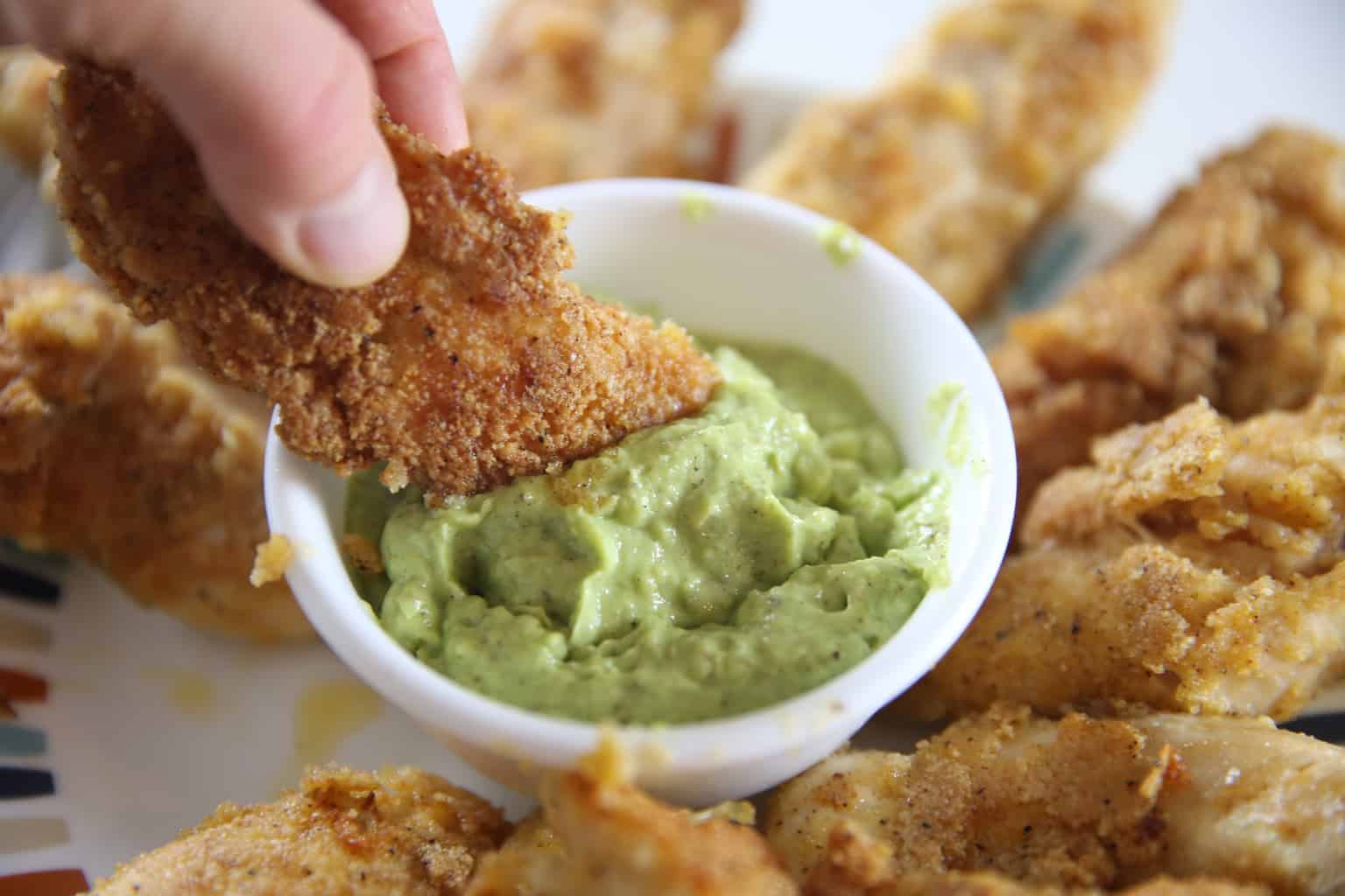 Homemade chicken strip being dipped into whole 30 sauce.