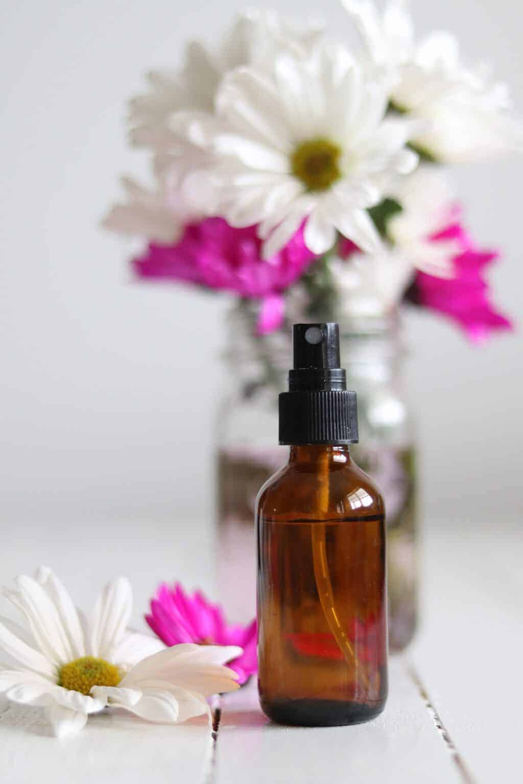 Essential oil spray bottle with fresh flowers in background.