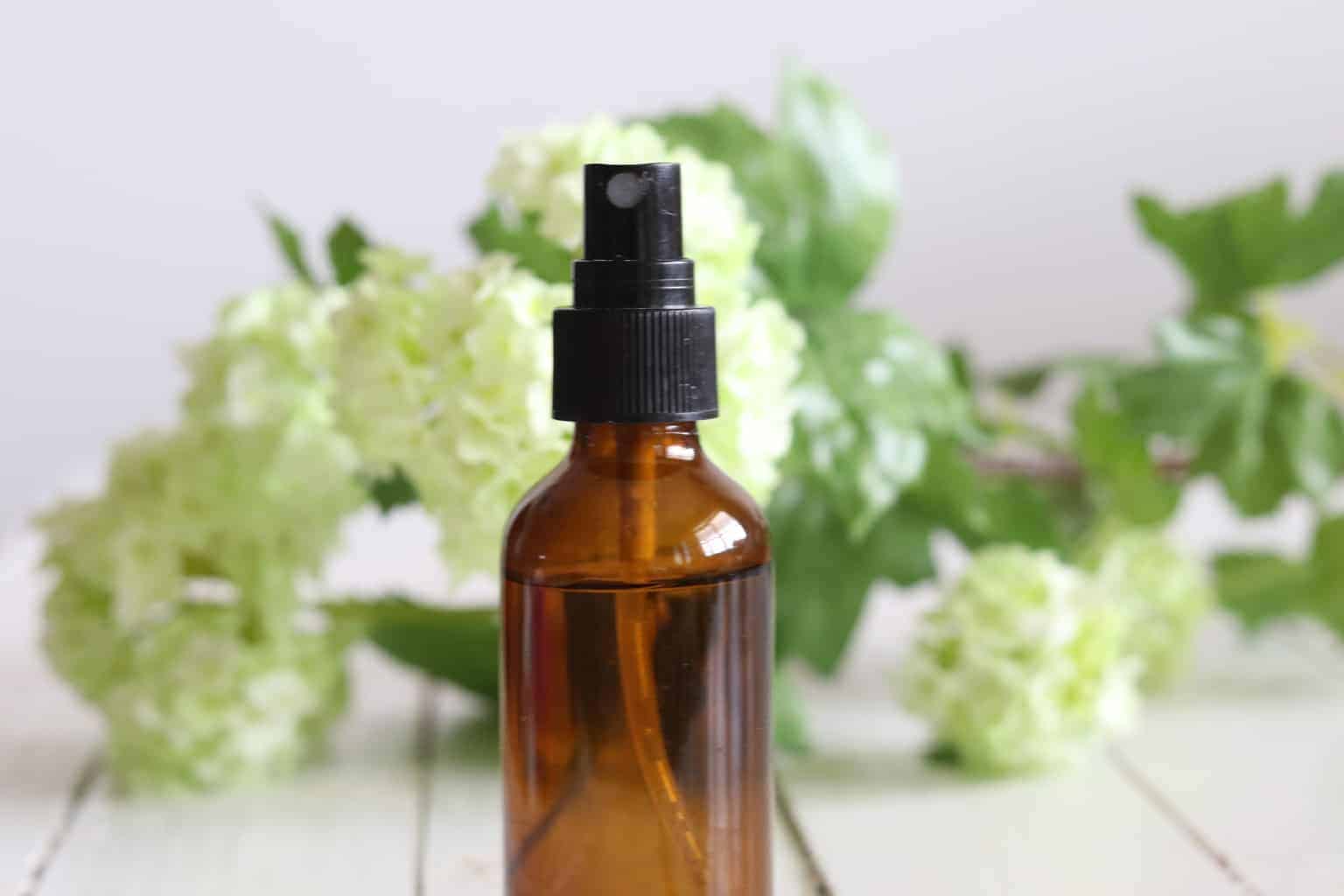 A essential oil spray bottle with fresh flowers in the background. 