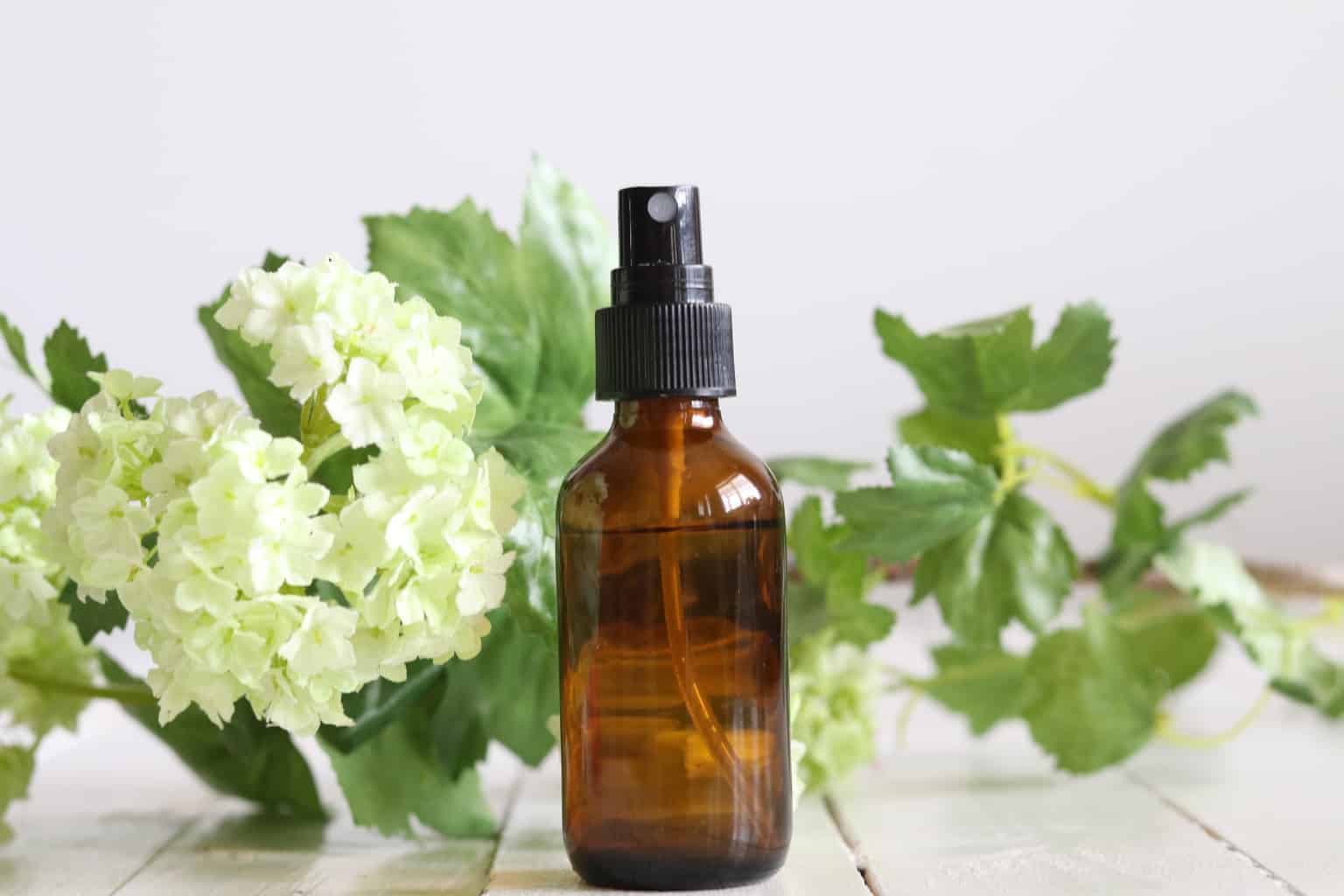 Essential oil spray bottle with flowers in the background.
