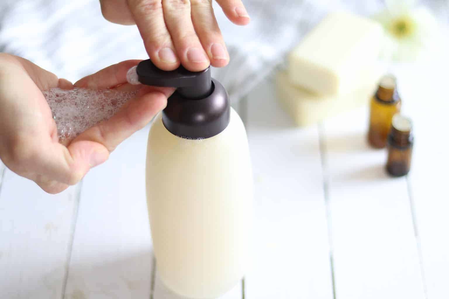 Homemade shampoo on wooden table with essential oil bottle and soap bar.