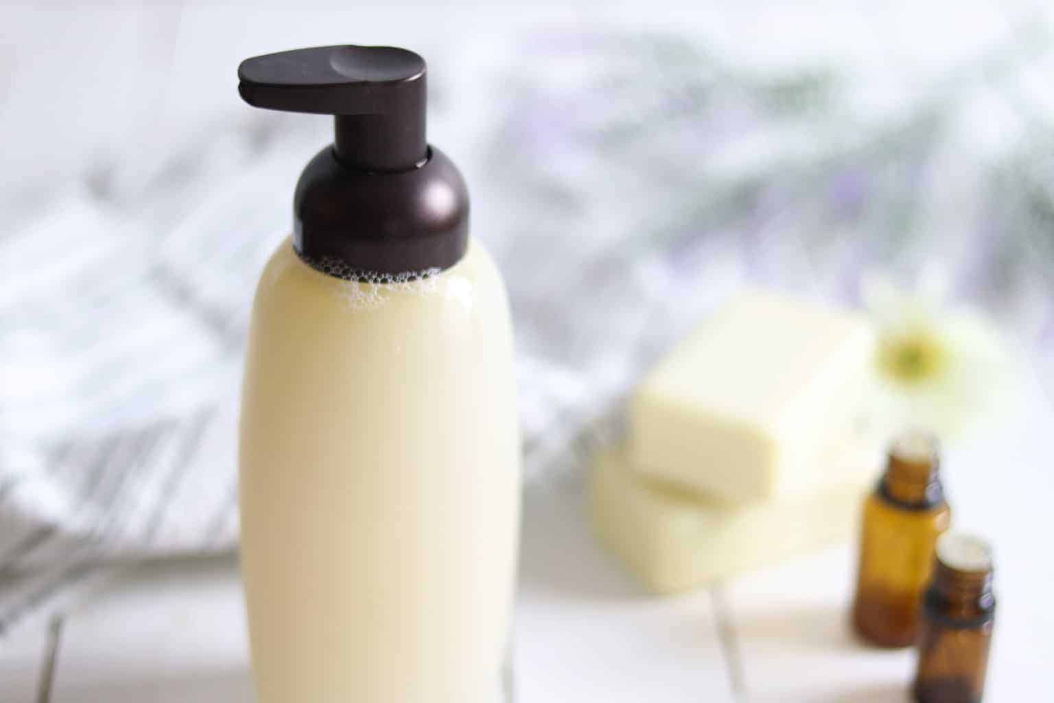 All-natural shampoo dispenser with homemade shampoo and essential oil bottles on white shiplap.