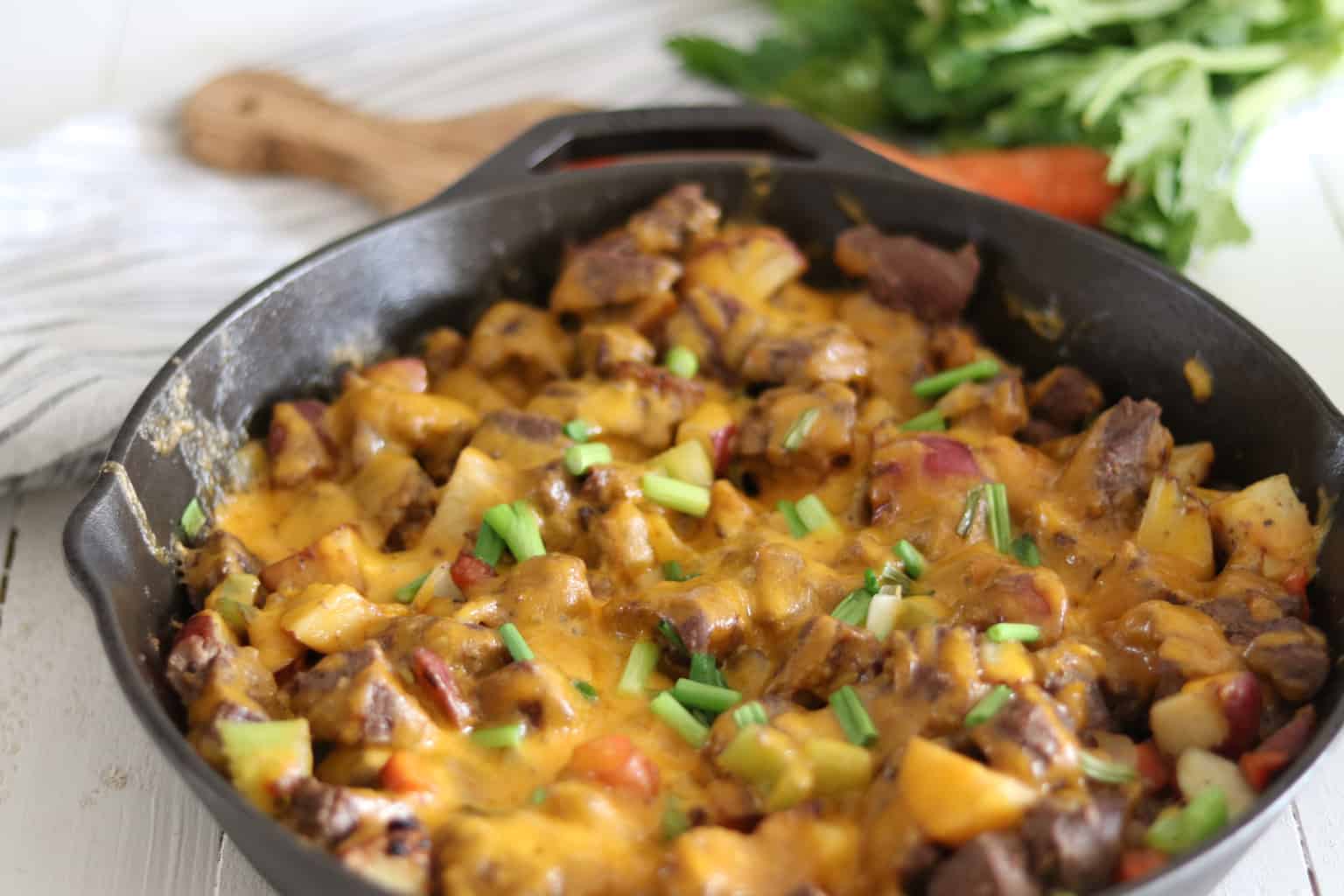 Cheesy cast-iron skillet melt with steak on wooden table.