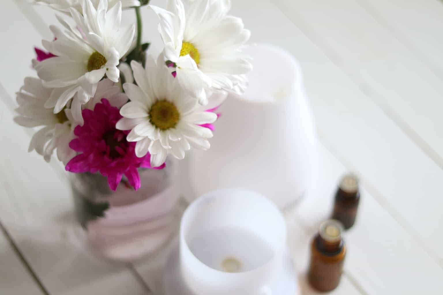 Fresh flowers in glass jar near essential oil bottles and oil diffuser.