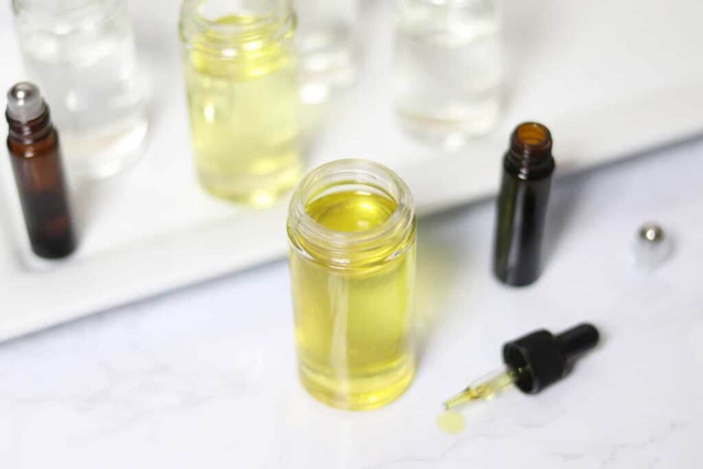 Fractionated coconut oil on white shiplap with essential oil dropper and roller bottles.