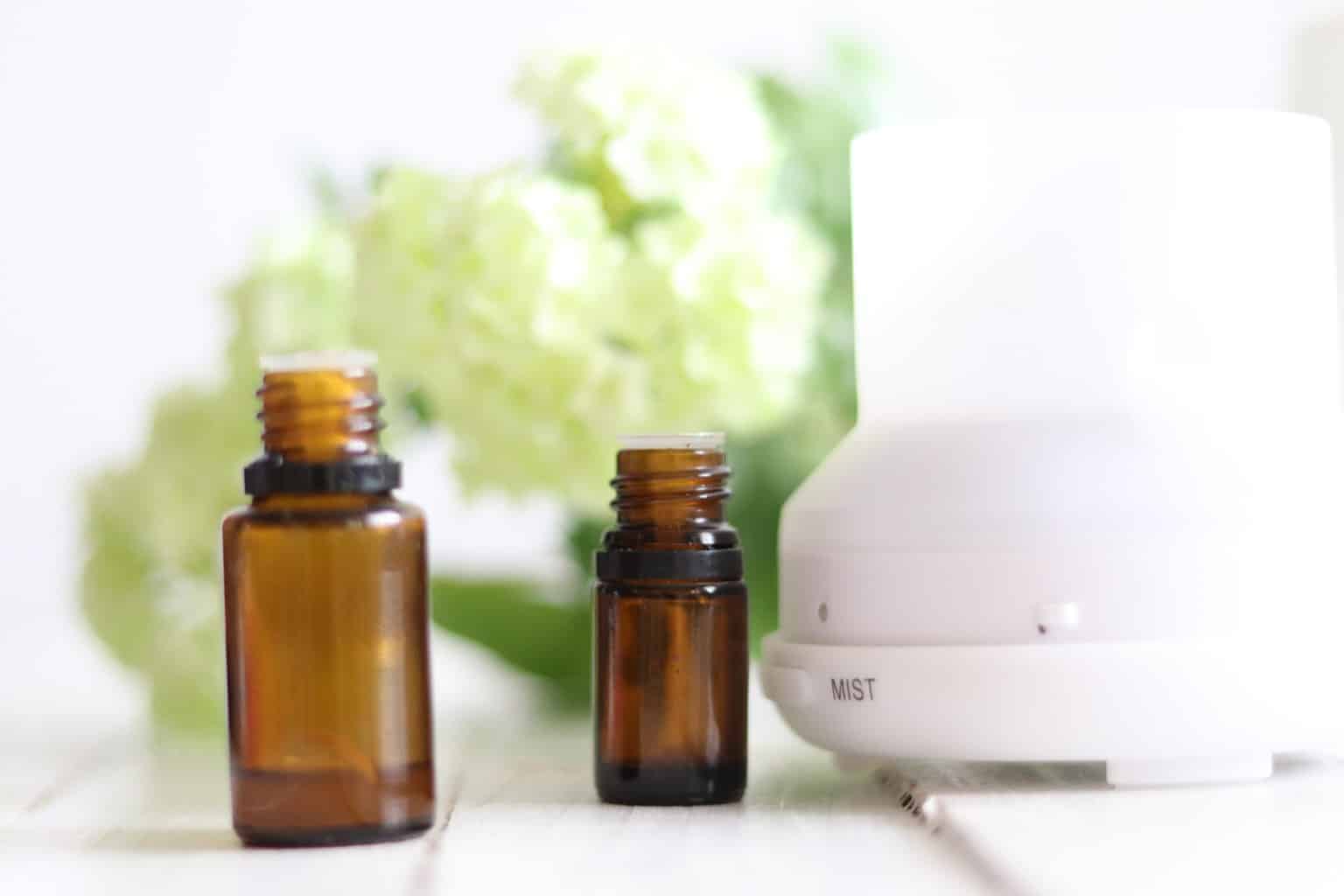 Essential oil bottles with flowers and oil diffuser in background.