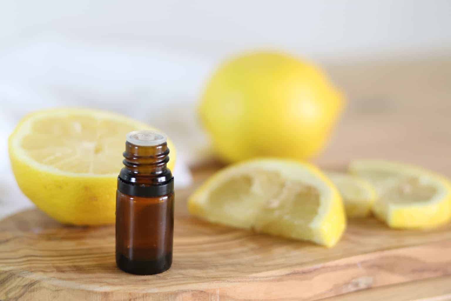 Essential oil bottle on wooden board with fresh lemons in background.