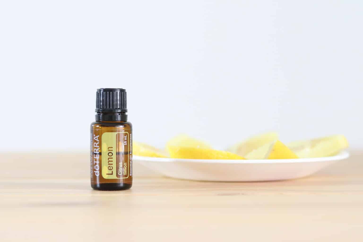 Lemon essential oil bottle with a plate of fresh lemon slices in background.