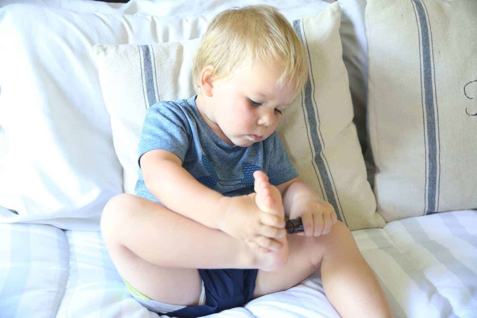 A little boy putting a roller bottle essential oil on his feet.